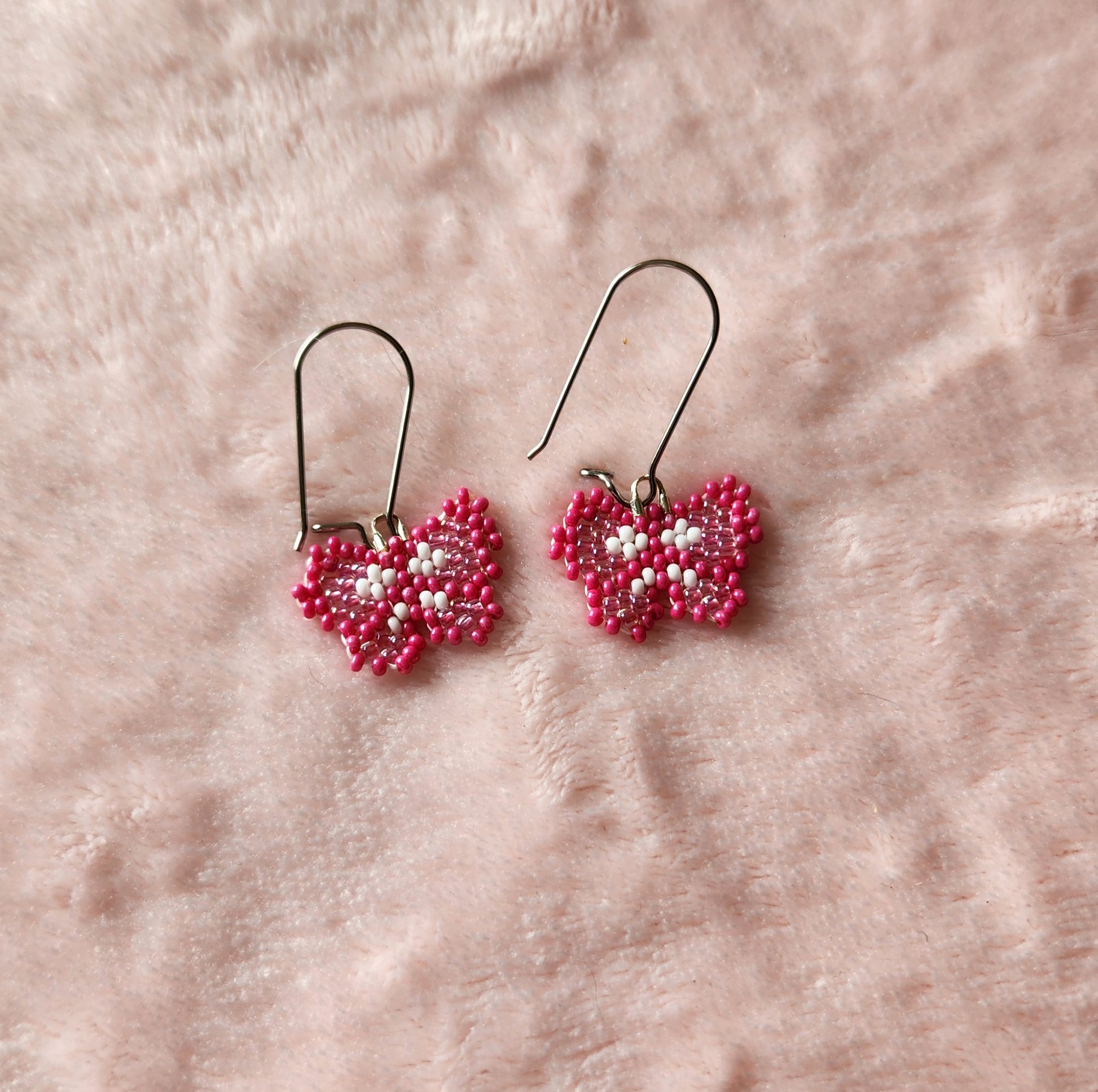 Fully beaded dark pink, light pink, and white seed bead earrings on kidney hooks, on a pink furry background.