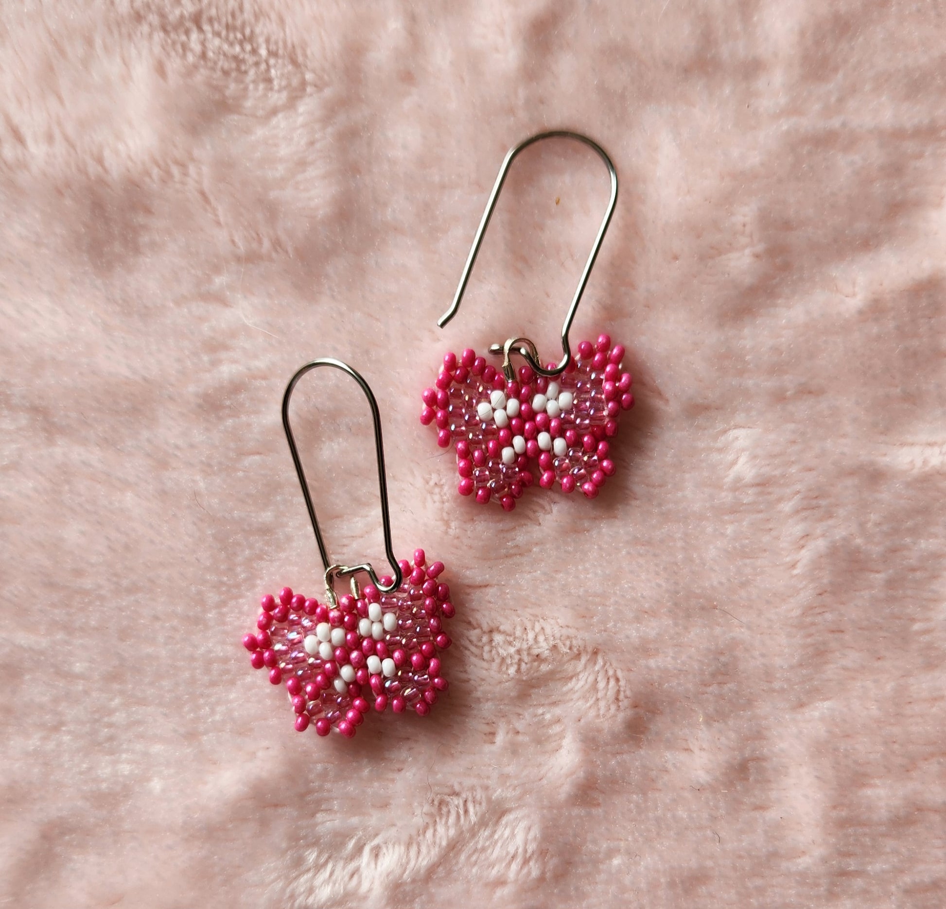 Fully beaded dark pink, light pink, and white seed bead earrings on kidney hooks, on a pink furry background.