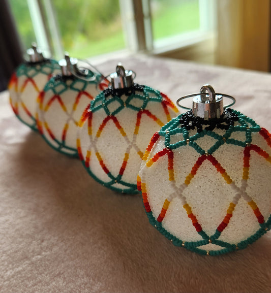 4 Christmas ornaments adorned with a netted beading design in turquoise, red, orange and white. On a pink furry background.